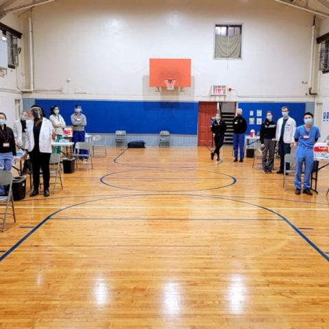Picture of health care professionals standing in a vaccination site set up in a gym